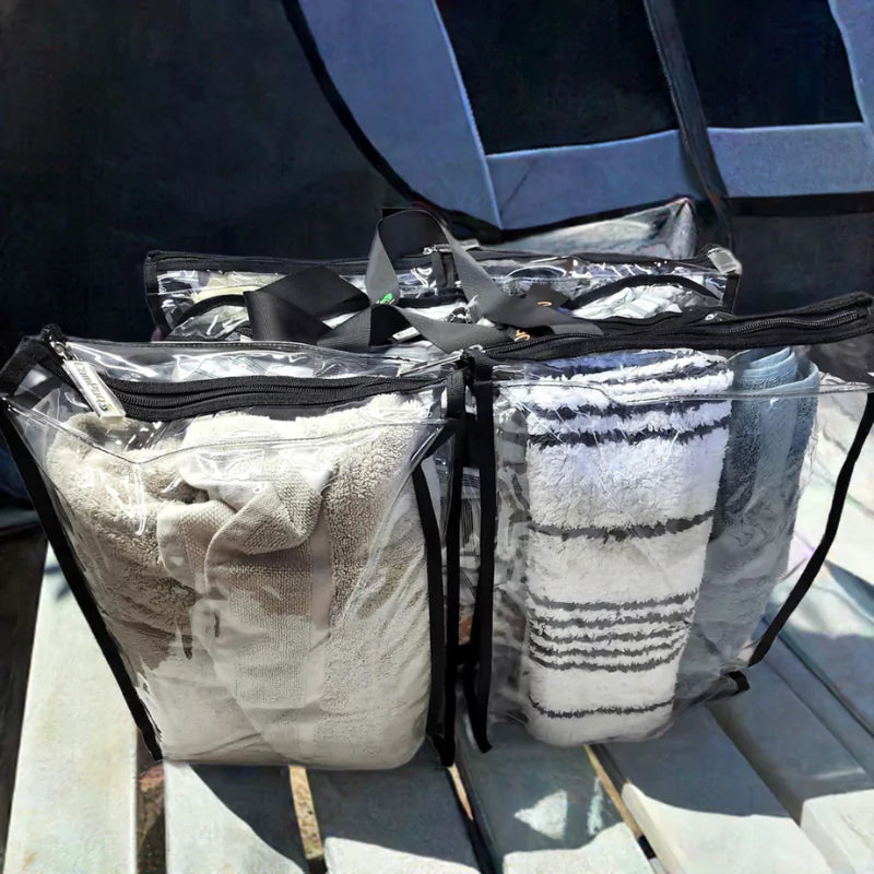 Large black trim clear camping bag packed with with linen beside tent