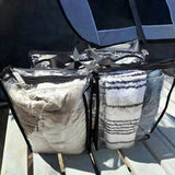 Large black trim clear camping bag packed with with linen beside tent