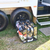 Large black trim clear camping bag with filled with camping clothes sitting on ground outside camper trailer