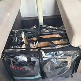 Large black trim clear camping bag with packed with clothes sitting on floor underneath camper trailer table
