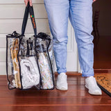Person standing on deck at front door of holiday house holding large black trim clear camping bag with packed with clothes