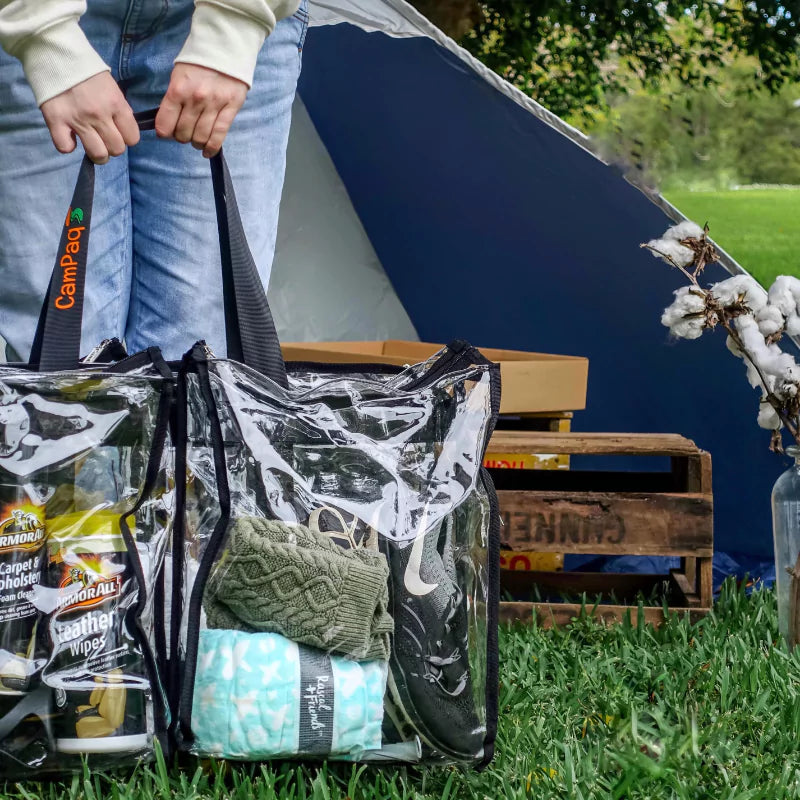 Person standing in front of tent outdoors holding large black trim clear camping bag filled with camping gear