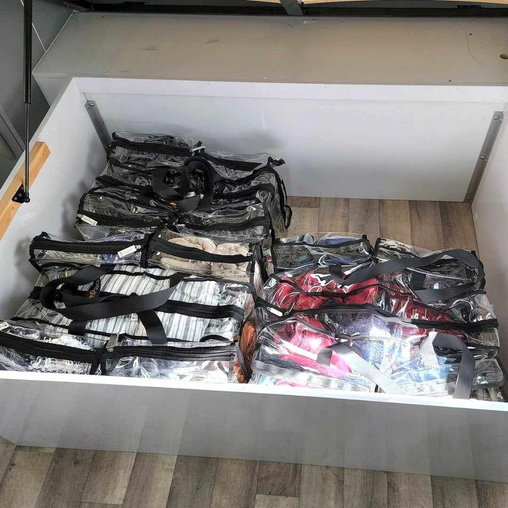 Three large black campaq clear bags packed with linen and shoes sitting under caravan bed