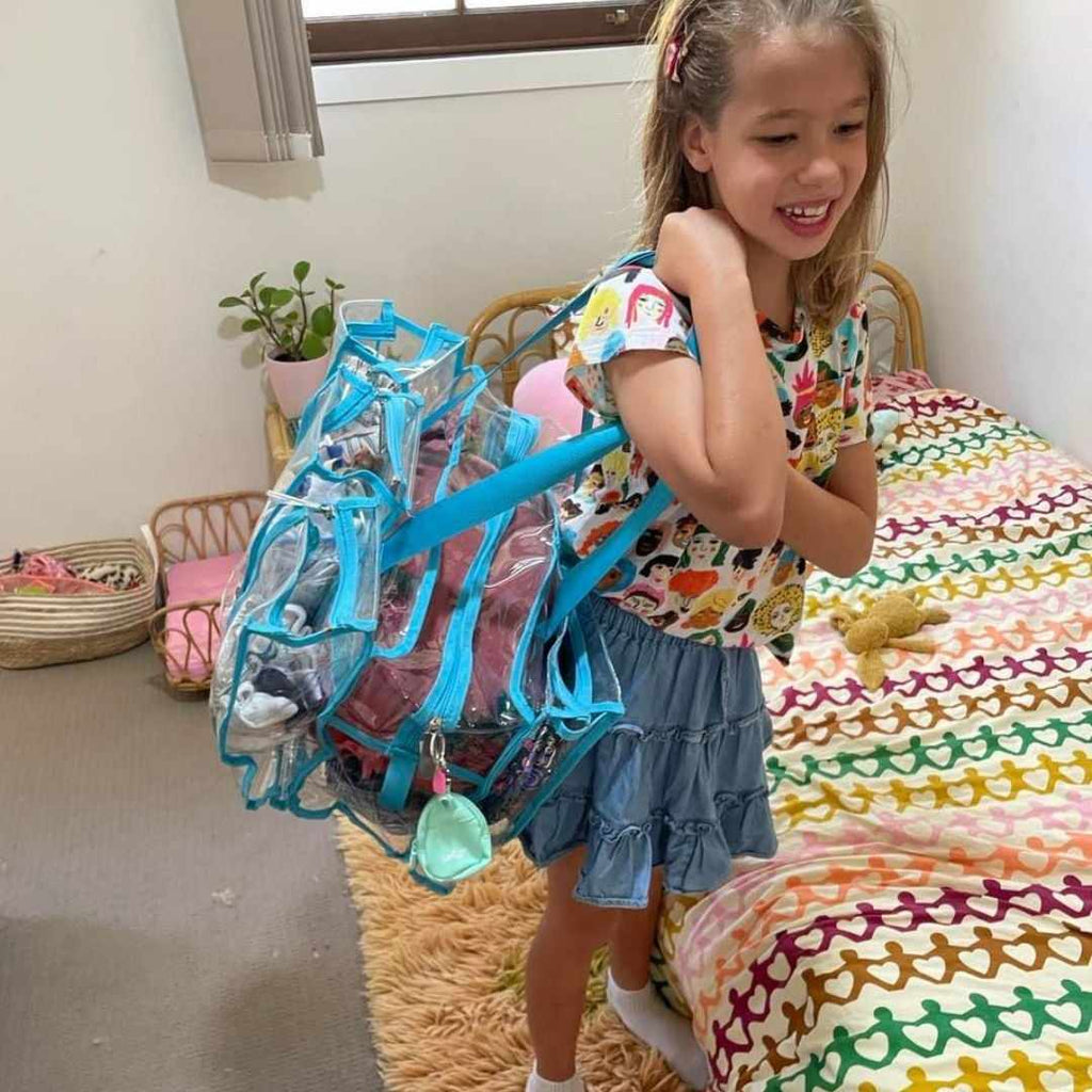 Girl smiling with blue medium CamPaq clear bag over her shoulder filled with clothes and toys