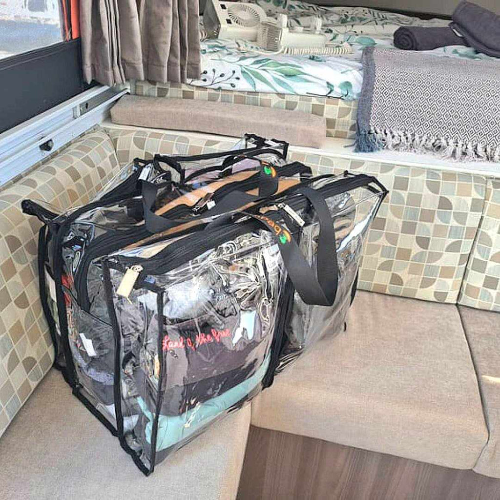 Large black CamPaq clear bag full of clothes sitting on couch seat in camper trailer