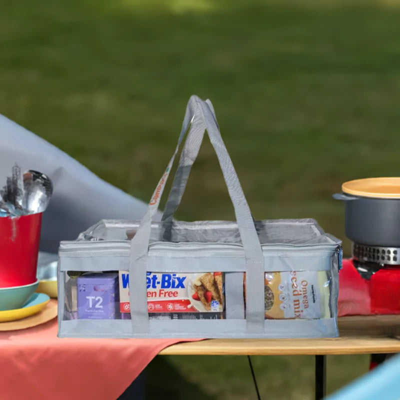 Grey clear under bed CamPaq storage bag packed with pantry items sitting on picnic table