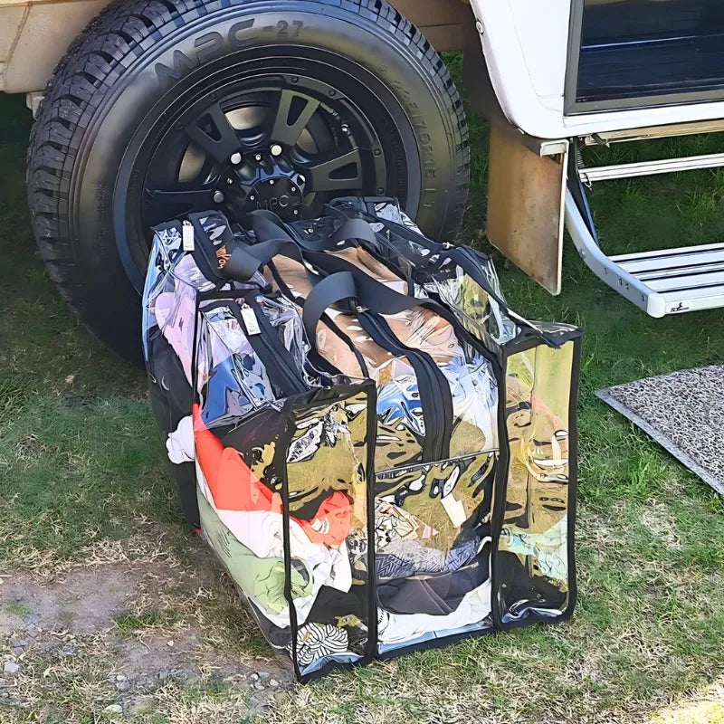 Large black clear camping bag with gear on ground beside caravan