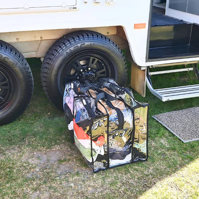 Large black trim clear camping bag with filled with camping clothes sitting on ground outside camper trailer