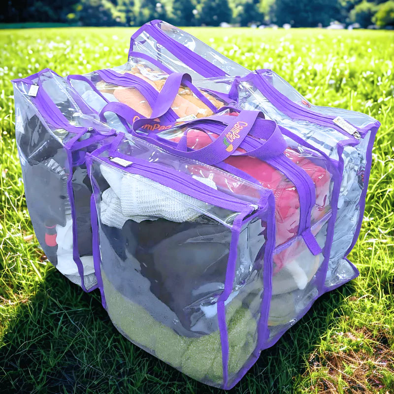 Large purple trim clear CamPaq camping bag containing clothes on a grassy field