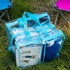 Medium clear blue camping bag with books and towels on grass beside kids camp chairs