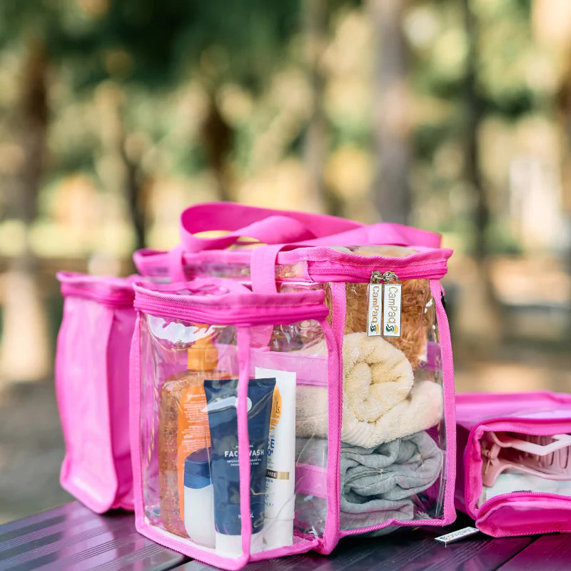 Clear hot pink CamPaq toiletry bag with clear sections filled with toiletries  and detachable opaque pocket