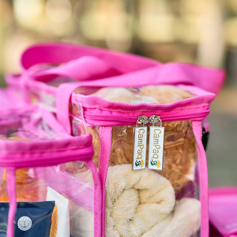 Clear hot pink CamPaq toiletry bag with a clear compartment containing towels and visible zipper tags CamPaq label.