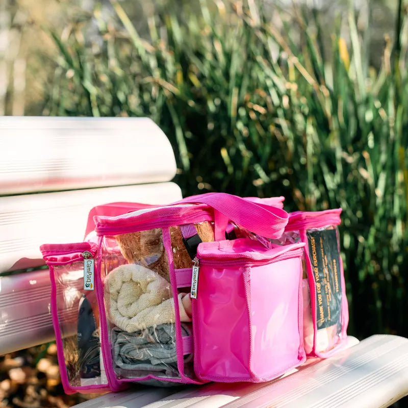 Hot pink CamPaq clear toiletry bag filled with towel and toiletries and opaque pocket sitting on seat