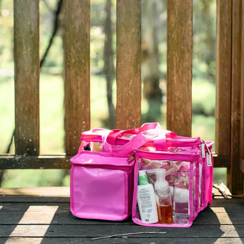 Hot pink clear CamPaq clear toiletry bag filled with toiletries sitting on wooden floor showing opaque pocket